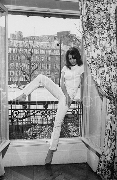 Actress Claudine Auger in ribbed t-shirt & tight pants, posing in large window of her elegant apt. w. street in bkgrd.