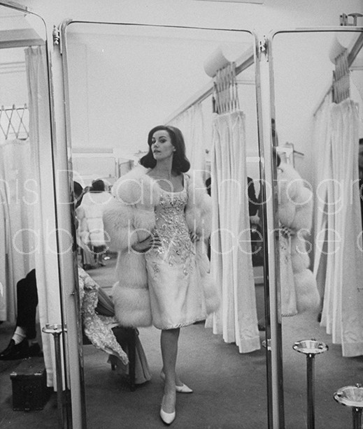 Reflection of actress Claudine Auger wearing white fur over elegant cocktail dress designed Pierre Balmain, as she poses in front of floor-length 3-way mirror at his salon.