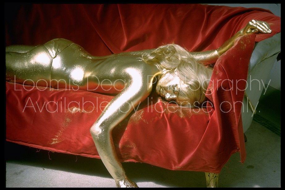 Actress Shirley Eaton lying dead of skin suffocation on red sofa after being painted gold fr. head to toe in scene fr. film "Goldfinger".