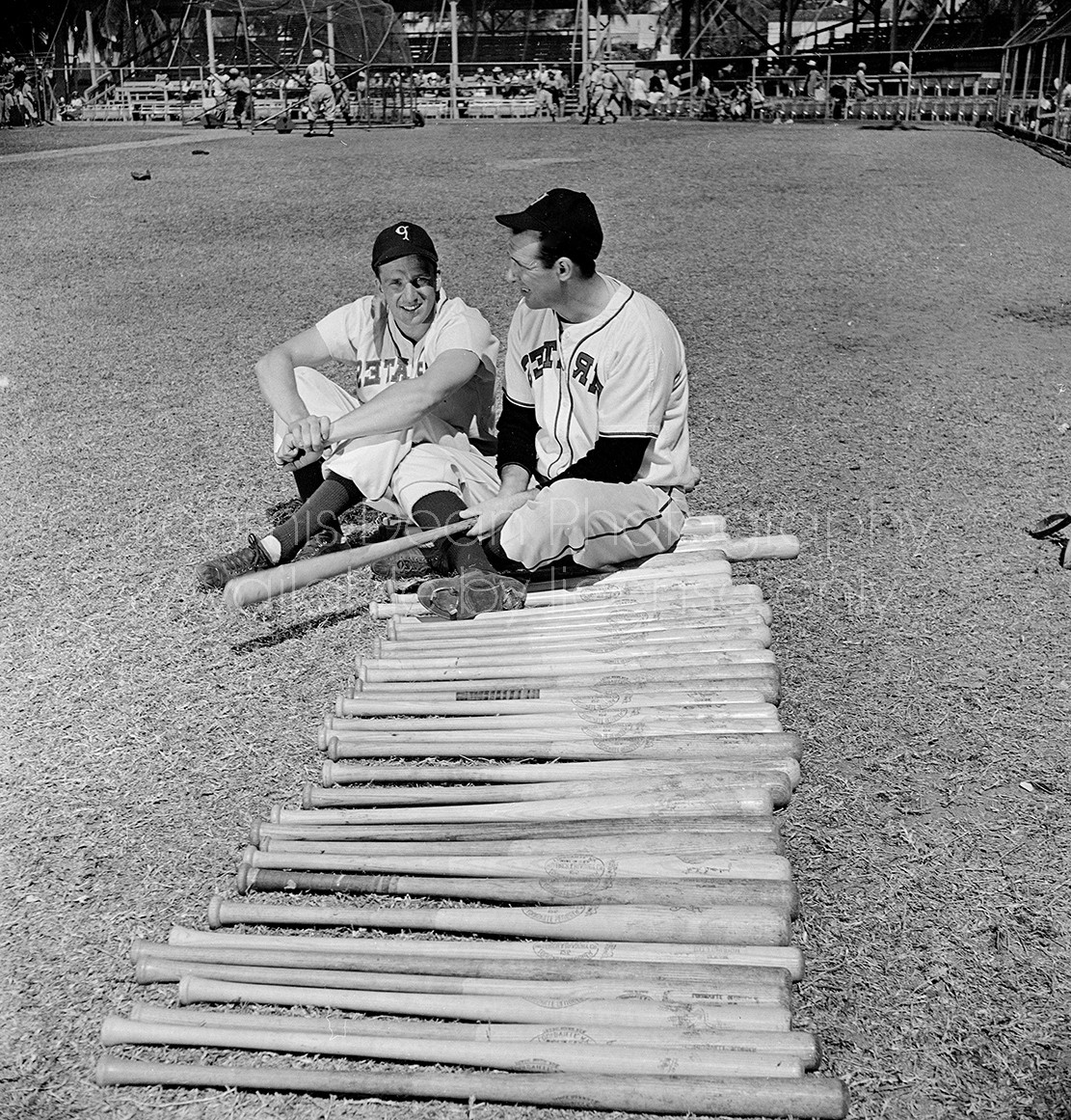 Pittsburgh Pirates players (L-R) Ralph Kiner & Hank Greenberg sitting next to a row of baseball bats during spring training.