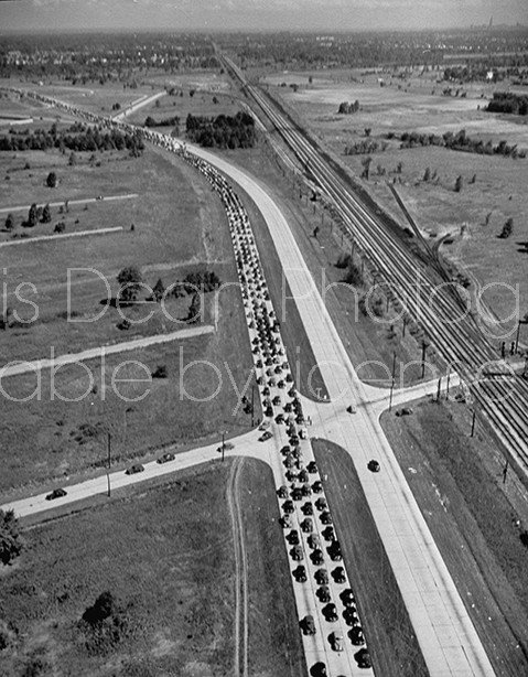 Aerial view of highway with steady stream of cars in 4 lanes, heading to the air show.