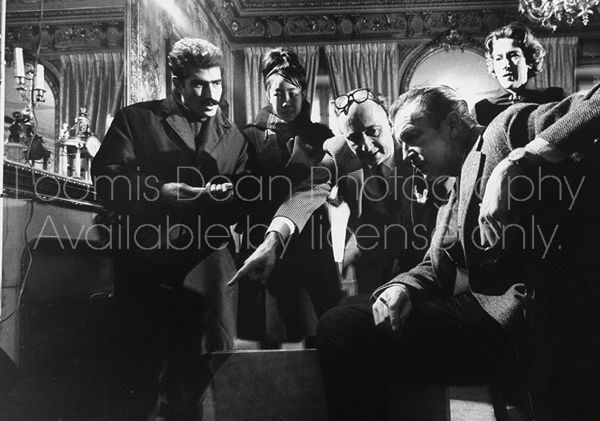Actor Vincent Price (R) sitting in a room among several others who are all observing a particular piece of artwork.