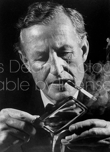 British mystery writer Ian Fleming looking at pirate coins with magnifying glass.