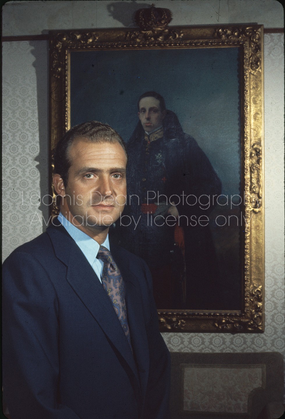 Spanish Prince Juan Carlos posing in front of portrait of his grandfather King Alphonso XIII, at home outside Madrid.