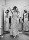 Actress Claudine Auger wearing a gorgeous, sleeveless, white brocade evening gown designed by Pierre Balmain, as she poses in front of floor-length 3-way mirror at his salon.