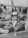 Actress Claudine Auger in two-piece bathing suit which features large clamshell designs as she poses sexily in front of fishing wharf backdrop.