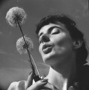 A model holding two healthy dry tufts of dandelion about to blow them.