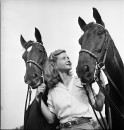 A woman standing with her two trick horses.