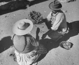 A man and woman crouching in the marketplace together.