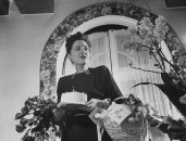 Dorothy Shaver holding flowers and a birthday cake with one candle on it.
