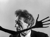 Portrait of sculptor Alberto Giacometti framed by reaching hand of one of his sculptures on display in museum.