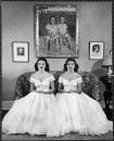 Debutantes Mary & Debbie Love posing on sofa in identical ball gowns on day of their debut into society.