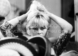 Actress Brigitte Bardot adjusts her hair in mirror while shopping for hats in Jean Barthet's millinery salons.