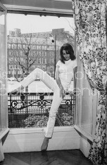 Actress Claudine Auger in ribbed t-shirt & tight pants, posing in large window of her elegant apt. w. street in bkgrd.