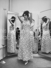 Actress Claudine Auger wearing a gorgeous, sleeveless, white brocade evening gown designed by Pierre Balmain, as she poses in front of floor-length 3-way mirror at his salon.