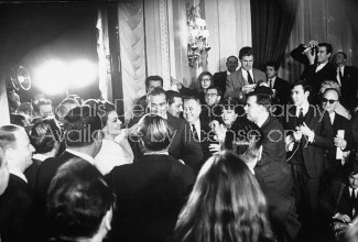 Actress Claudine Auger in white fur w. actor Sean Connery (C) being mobbed by newsmen & photographers at reception held in the Georges Cinq Hotel after the release of their movie "Thunderball".