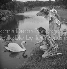 Two fashion models feeding a duck while modelling new cotton dresses.