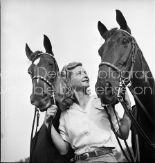 A woman standing with her two trick horses.