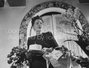 Dorothy Shaver holding flowers and a birthday cake with one candle on it.