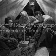 Director of "The Treasure of the Sierra Madre" John Huston (R) with the film's actors Humphrey Bogart (L) and his father Walter Huston (C), as they talk inside of lamplit tent while testing handmade scale.