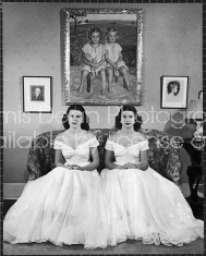 Debutantes Mary & Debbie Love posing on sofa in identical ball gowns on day of their debut into society.